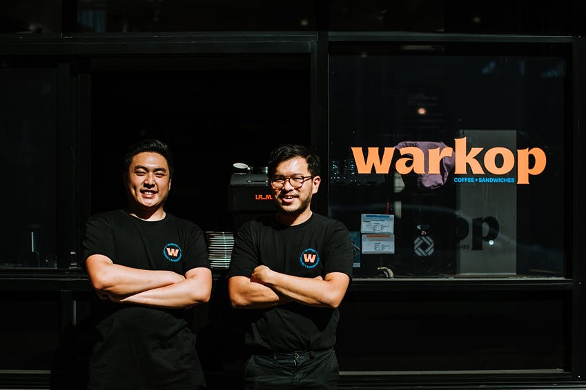Two people with their arms crossed out front of a shop.